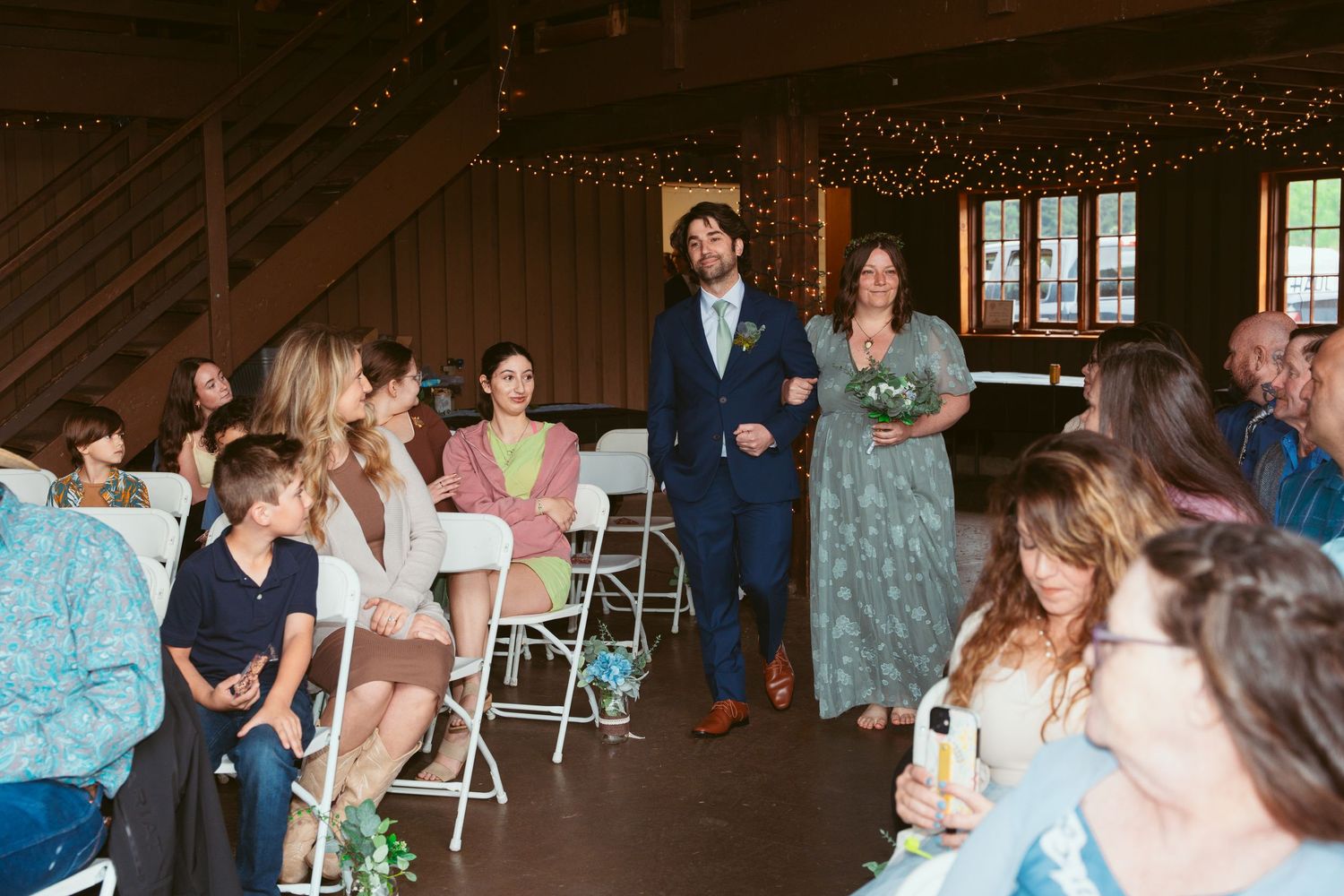 Guests gathered for a wedding celebration in a rustic barn with string light decorations.