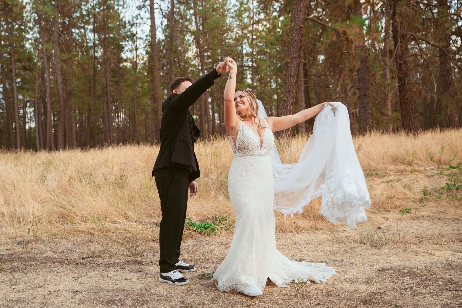 Wedding couple poses in a rustic field with pine trees creating a romantic forest backdrop.