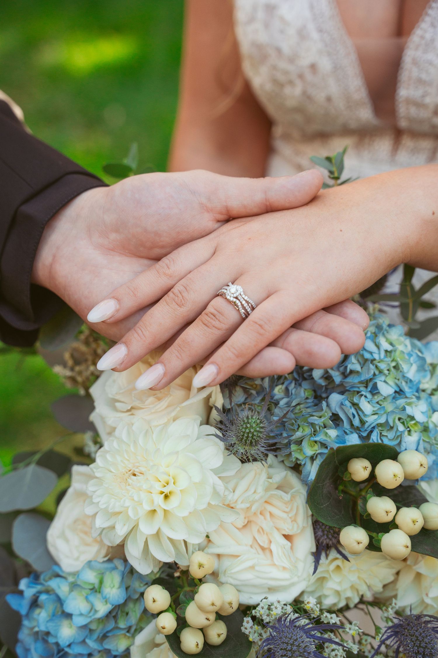 Close-up of hands with wedding rings resting on a blue and white floral bouquet.