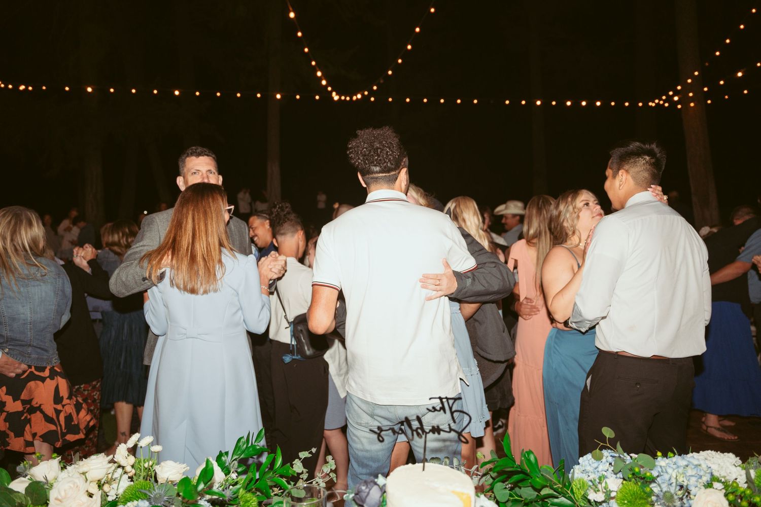 String lights illuminate outdoor wedding reception as guests mingle and dance.
