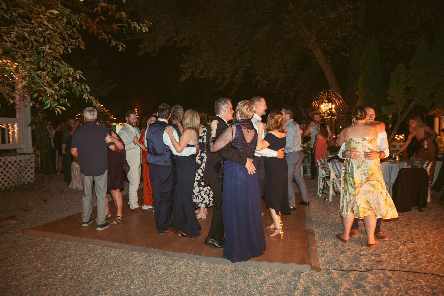 Guests mingling and dancing at outdoor wedding reception with string lights overhead.