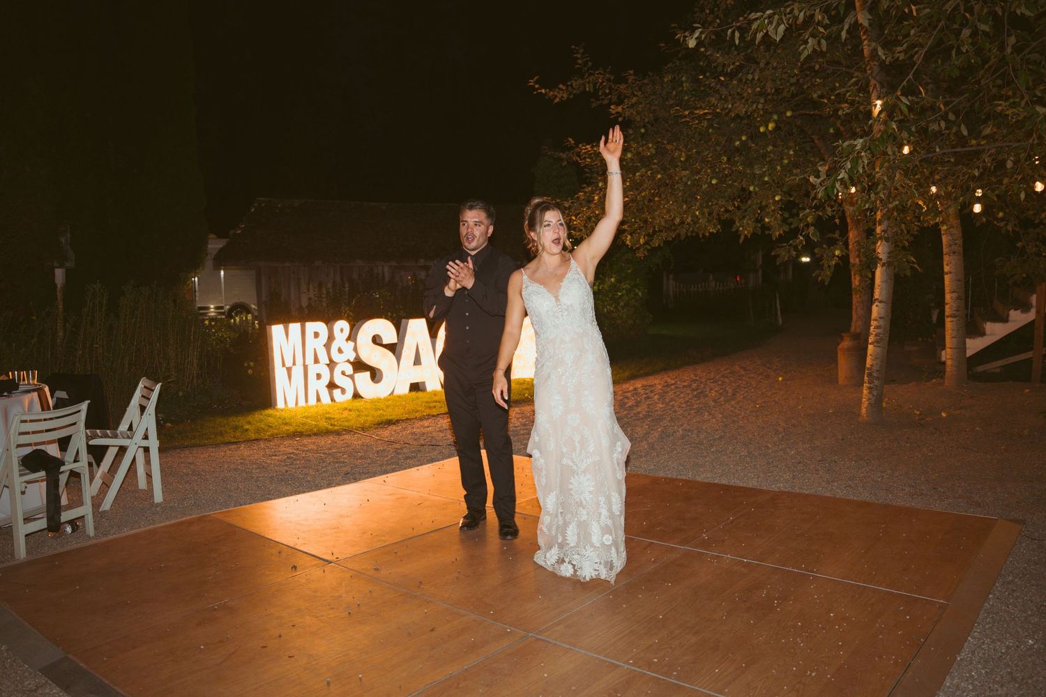 A couple poses in front of an illuminated sign at their nighttime wedding celebration.
