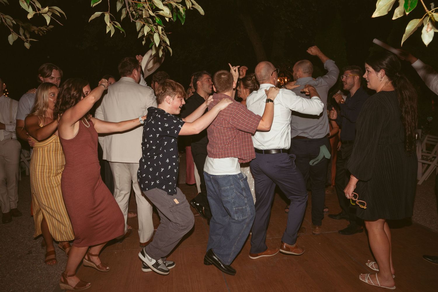 Large group of wedding guests performing a coordinated dance move at an outdoor reception.
