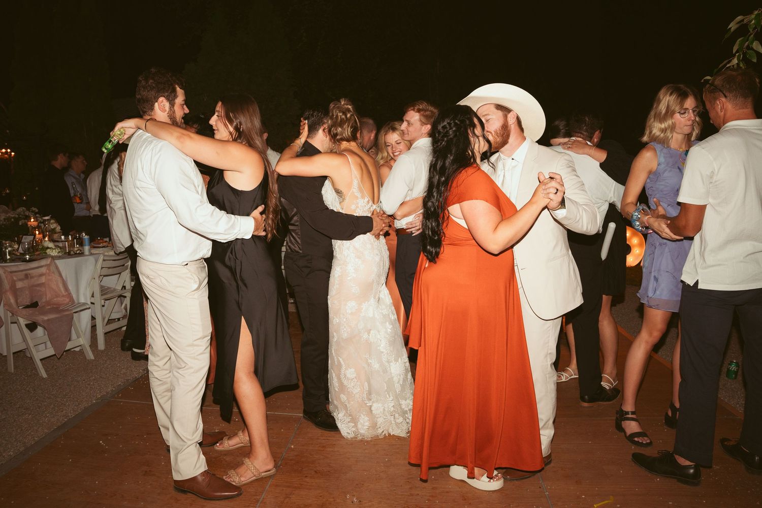 Wedding guests dancing in formal attire at outdoor evening celebration.