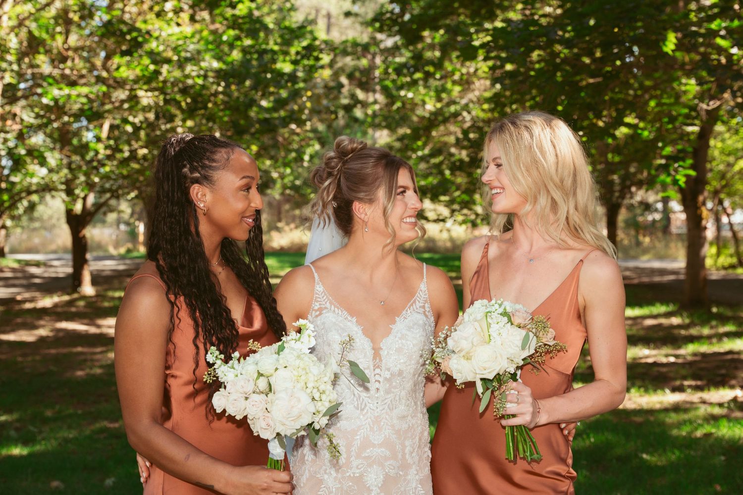 Wedding party in orange and white dresses pose together in a sunny garden setting.