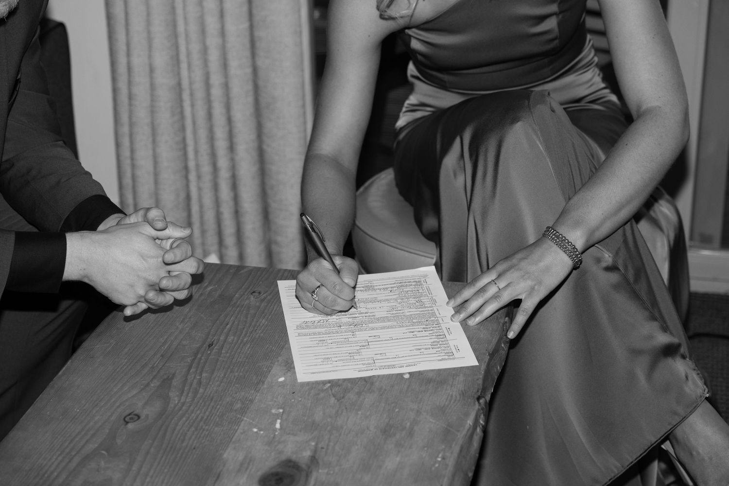 Close up of hands signing wedding documents on a wooden table.