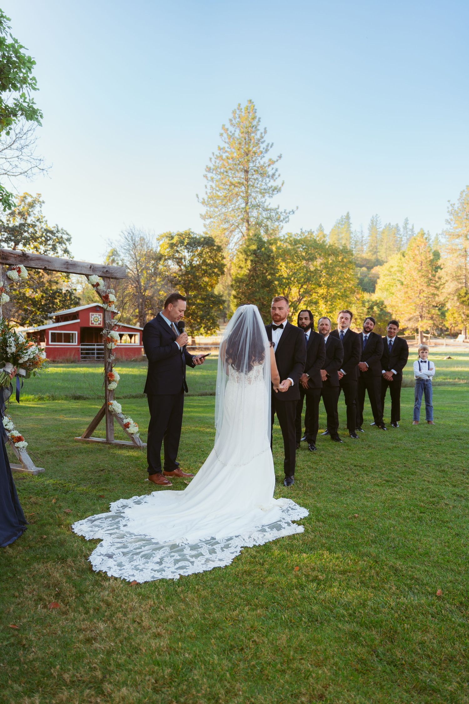 Wedding ceremony group poses on grassy lawn with fall trees in background.