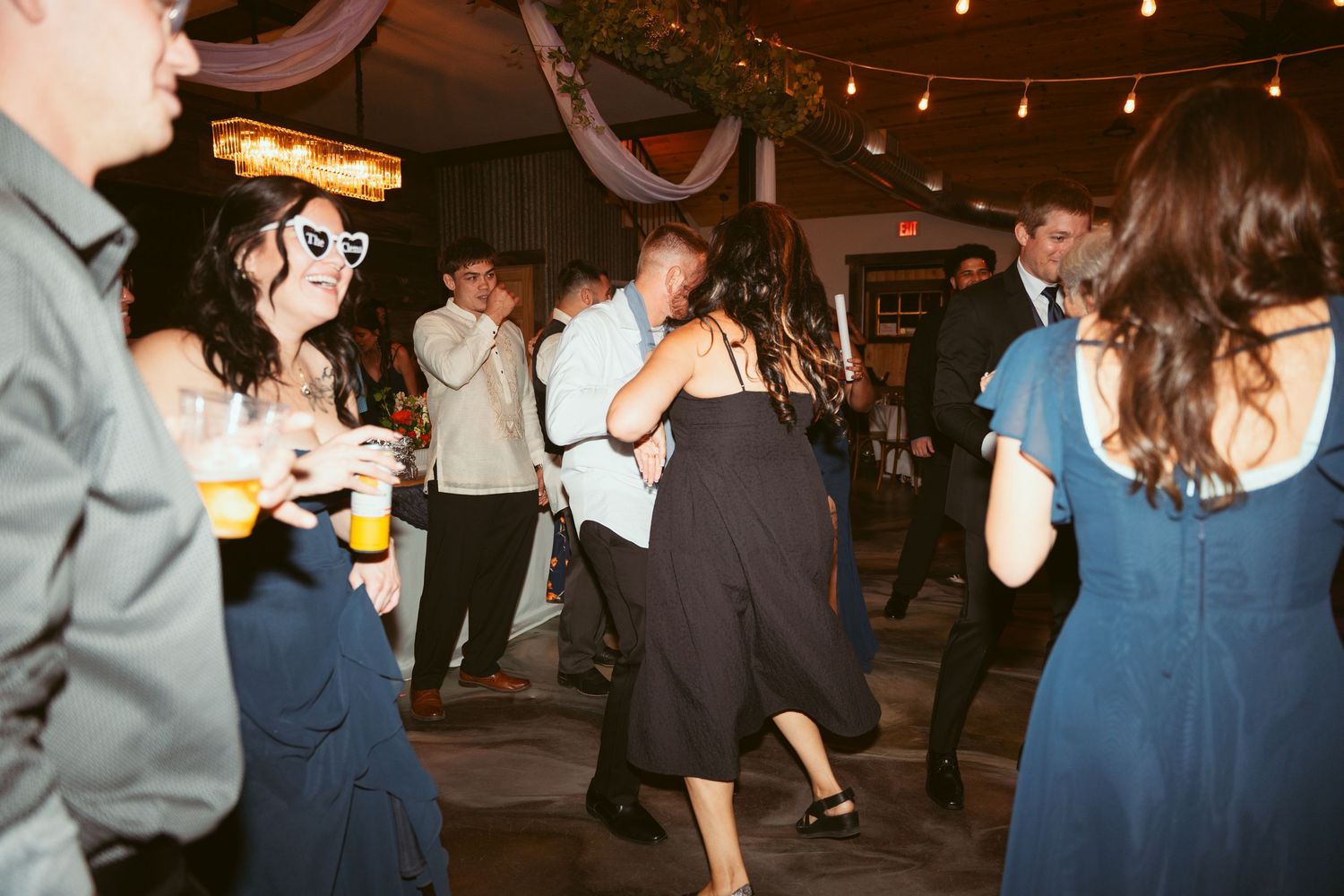 People dancing and celebrating at a dimly lit indoor party venue with string lights overhead.