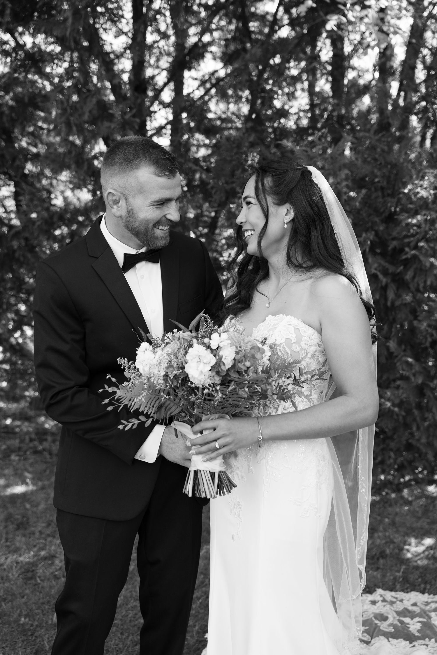 Black and white portrait of newlyweds sharing a joyful moment with bridal bouquet.
