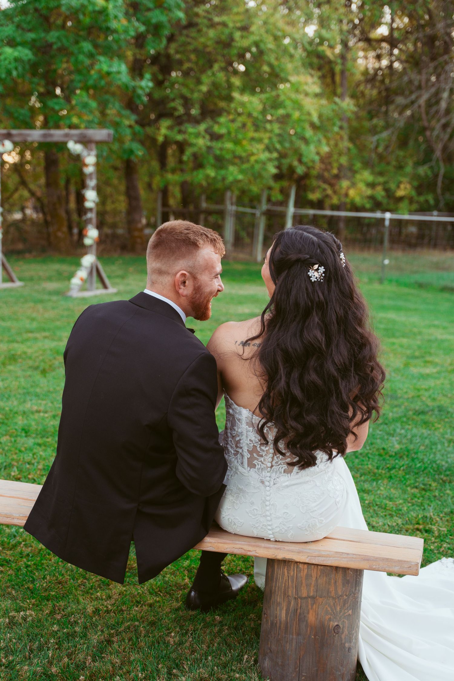 Couple sits together on rustic wooden bench in lush green garden setting.