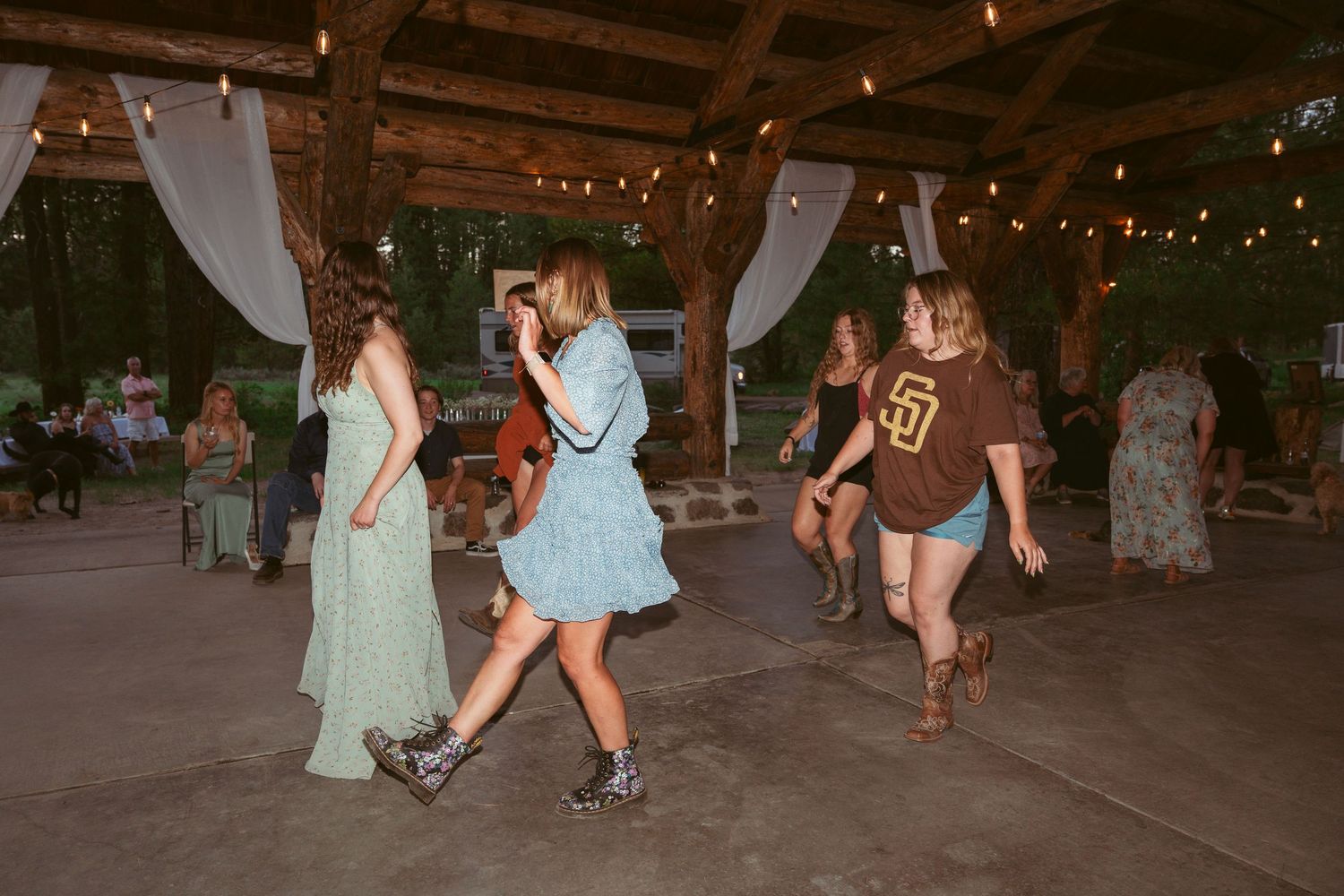 People dancing on a rustic wooden floor under twinkling lights at a celebration.
