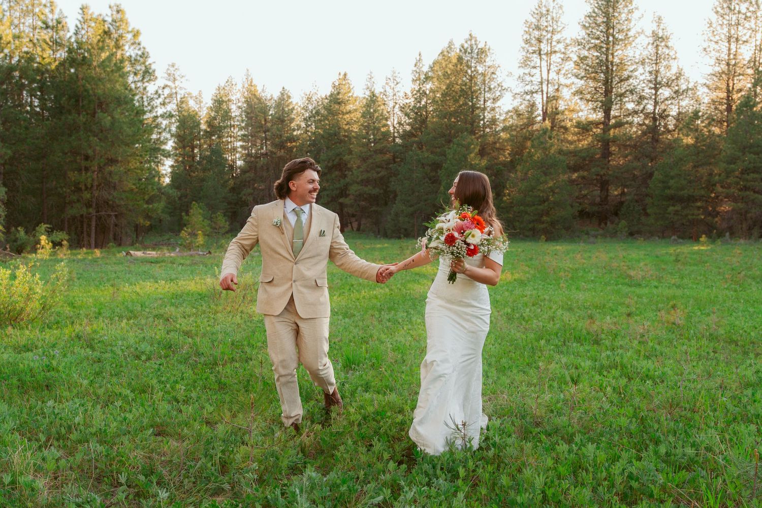 Joyful wedding couple runs hand-in-hand through a scenic meadow at golden hour.
