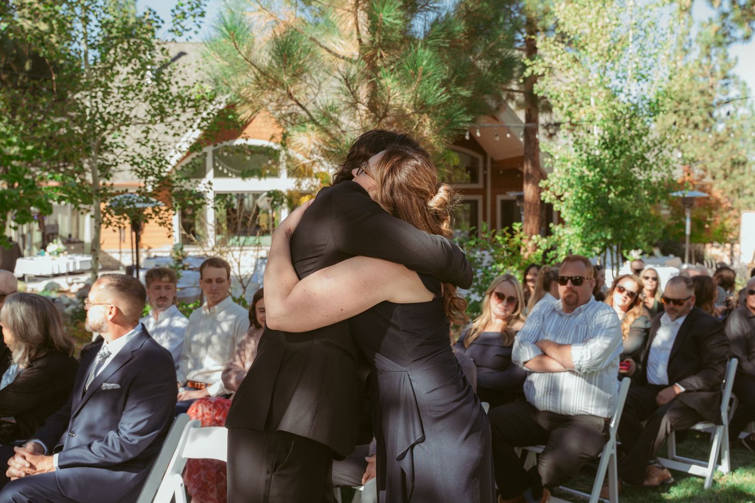 Emotional embrace shared during outdoor wedding ceremony while guests look on.