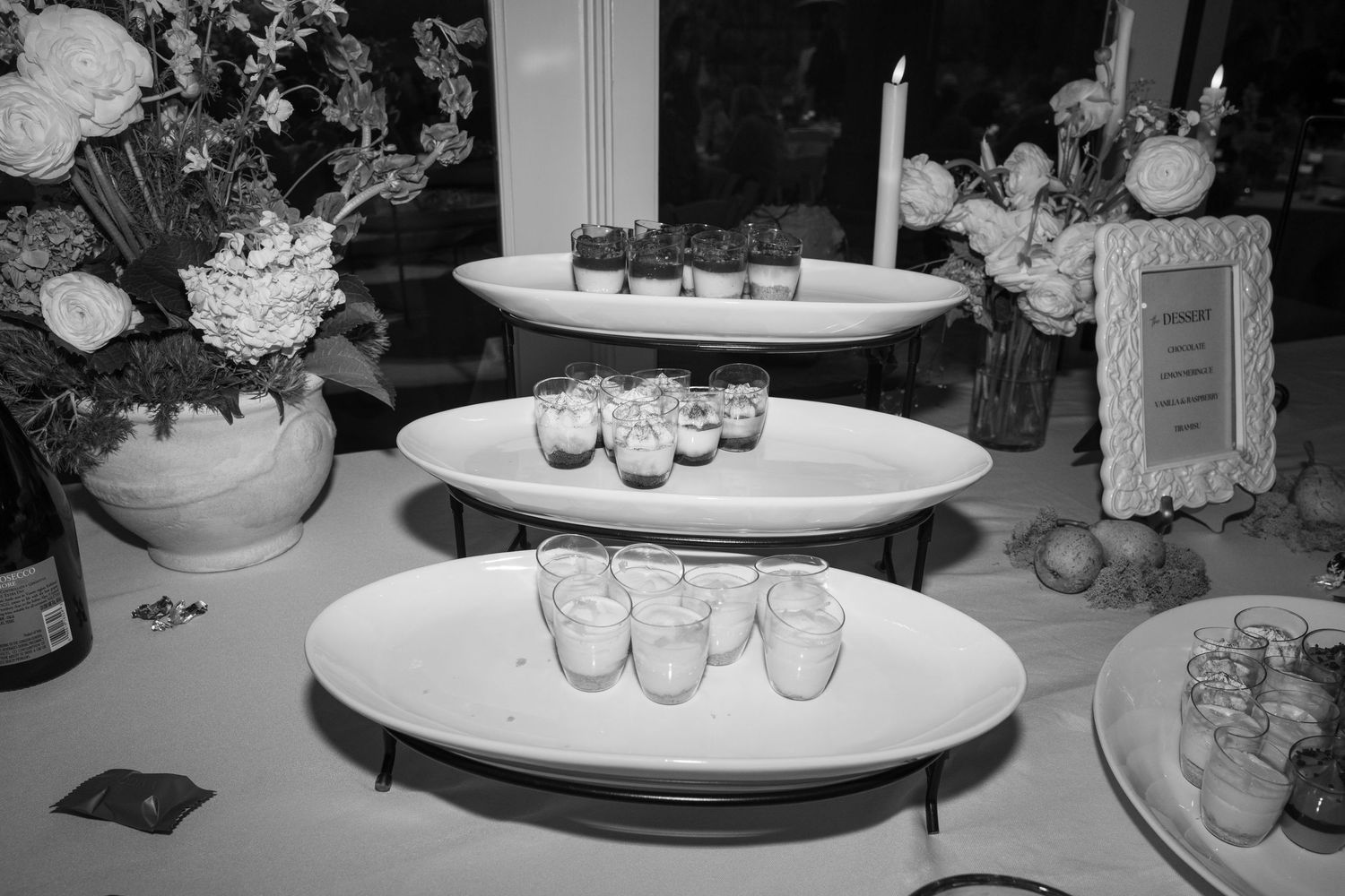 Elegant party setup with white floral arrangements and dessert displays on round tables.