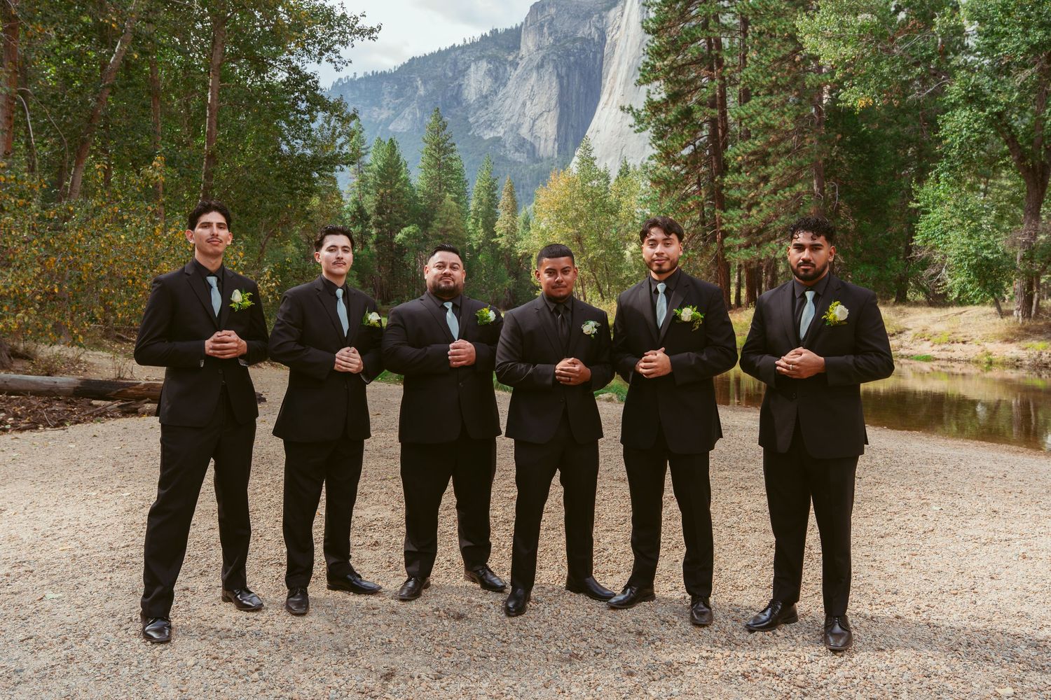 Wedding party in black suits striking playful poses against a mountain backdrop.