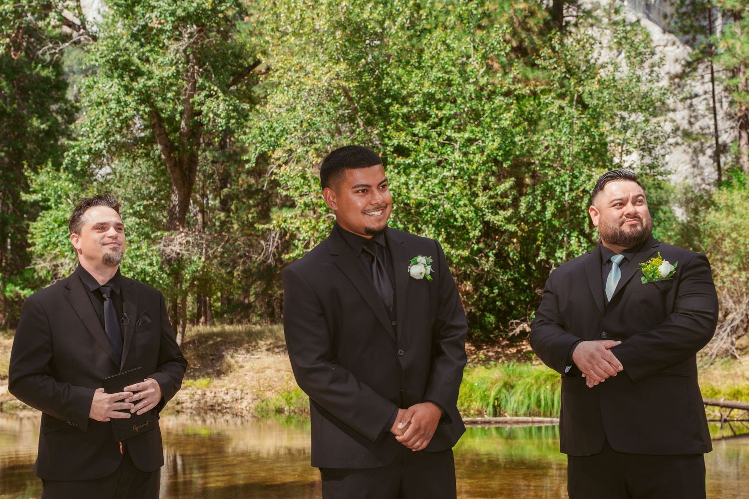 Groomsmen in black suits lined up outdoors with natural greenery backdrop in Yosemite.
