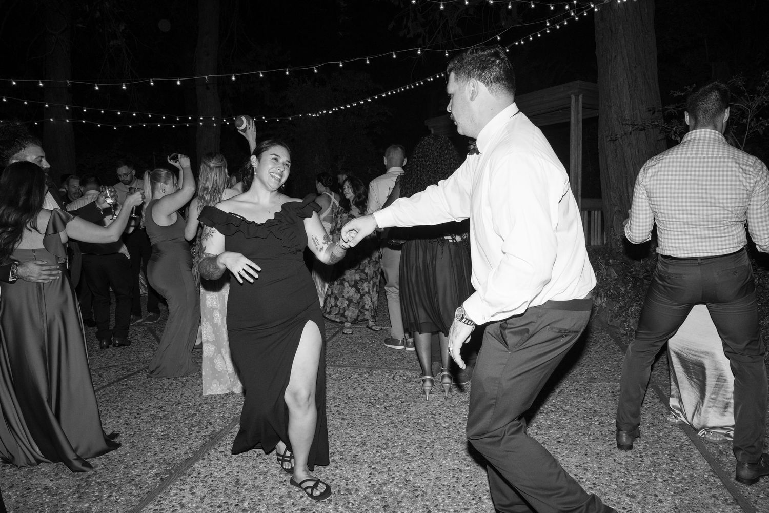 Guests dancing in rows at an outdoor wedding reception under string lights.