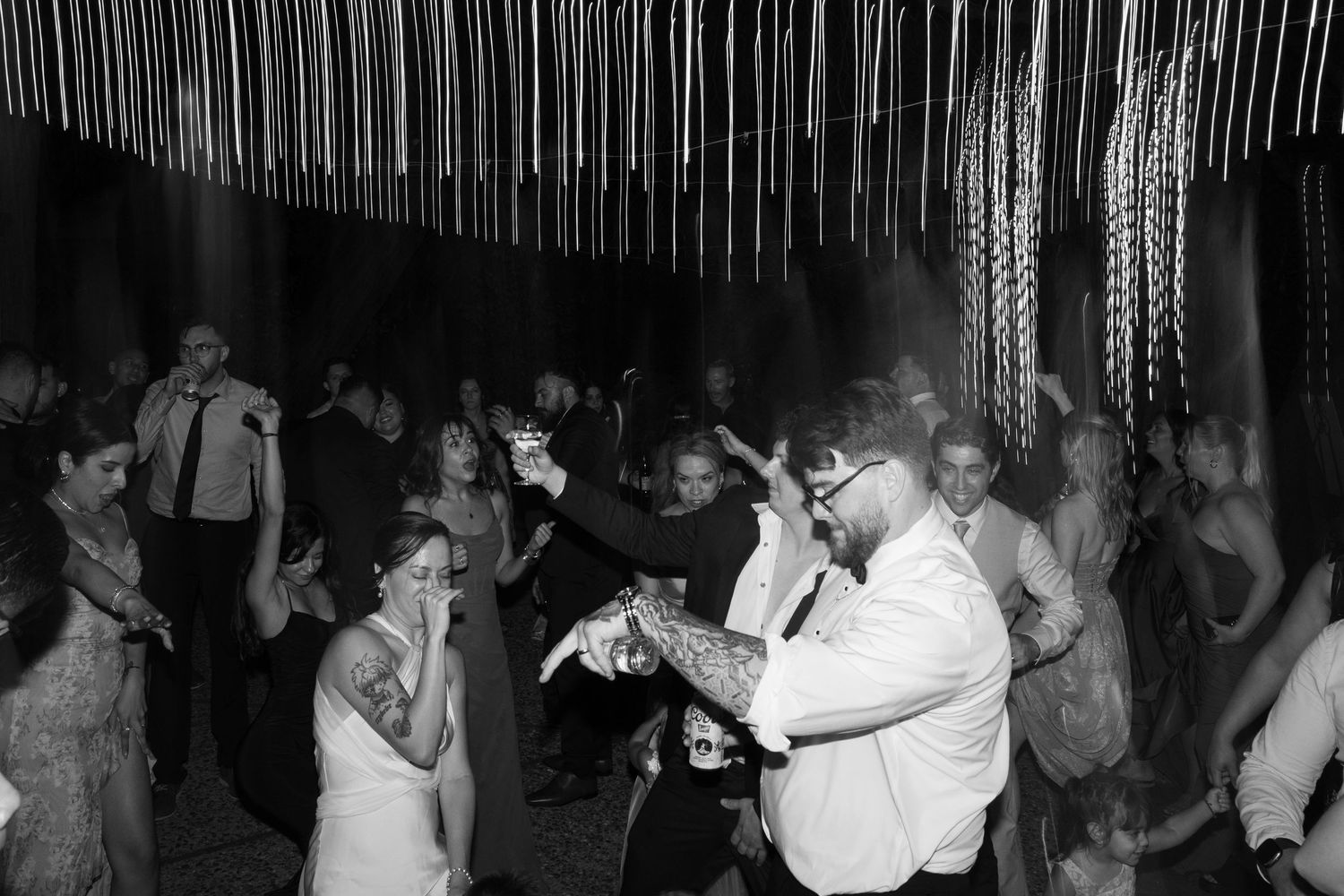 Black and white photograph showing people dancing together at a party or celebration in a dimly lit venue.