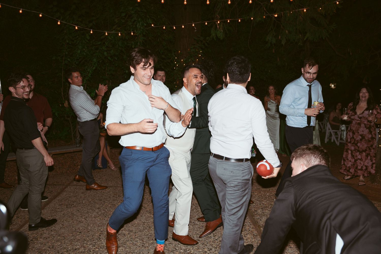 Wedding reception dance party with guests enjoying themselves under evening lighting.