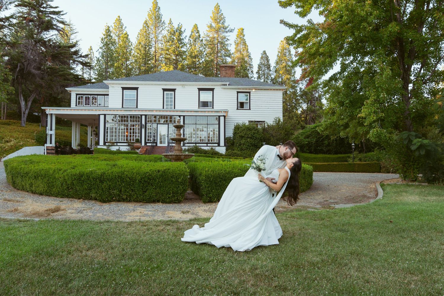 Wedding couple dancing and twirling on a grassy lawn with a house in the background.