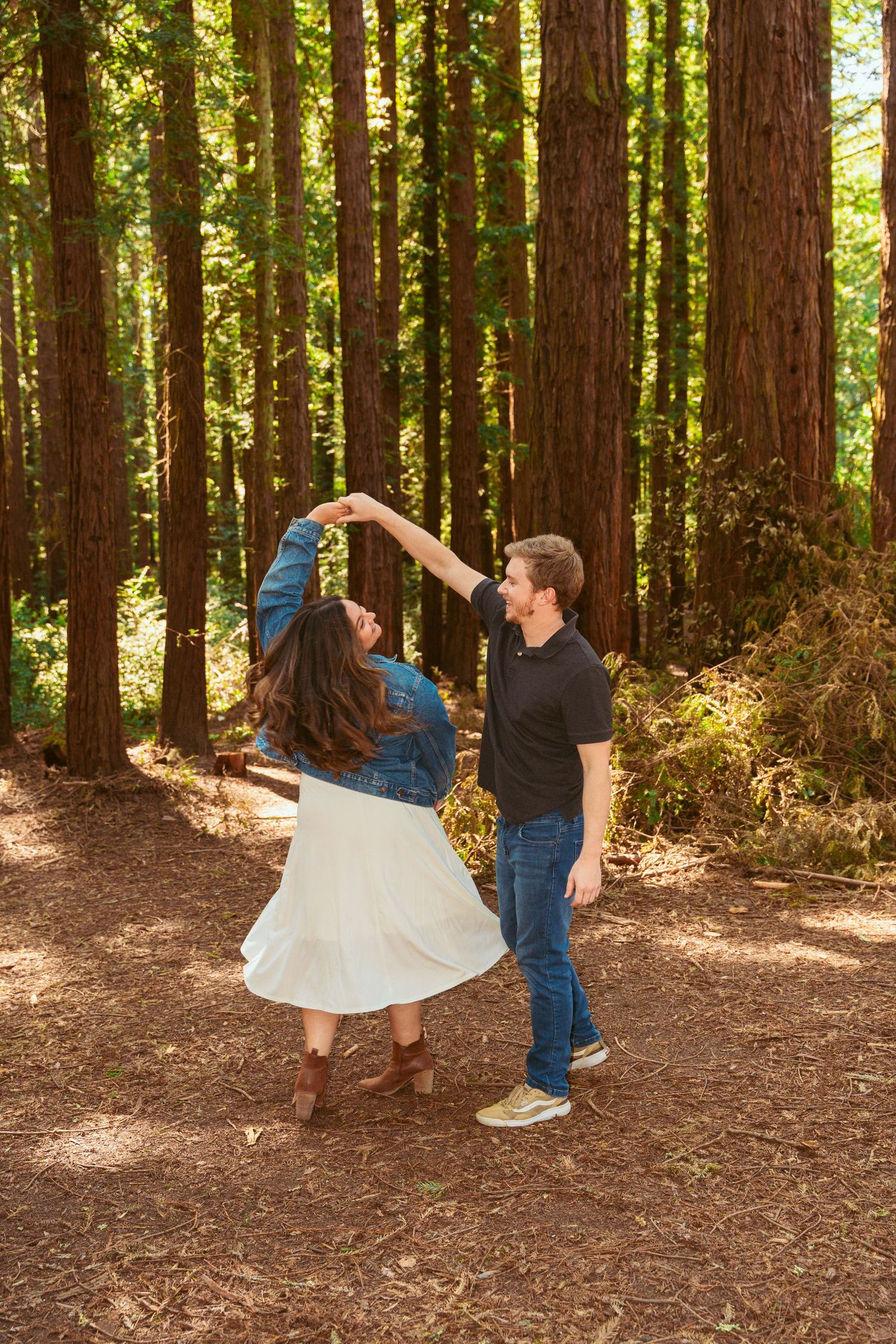 A couple performs a romantic dance dip pose surrounded by majestic redwood trees.