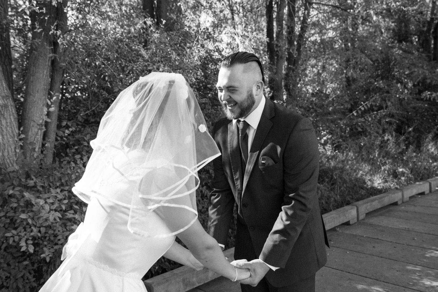 A romantic first look moment between newlyweds in a wooded outdoor setting with sunlight filtering through trees.