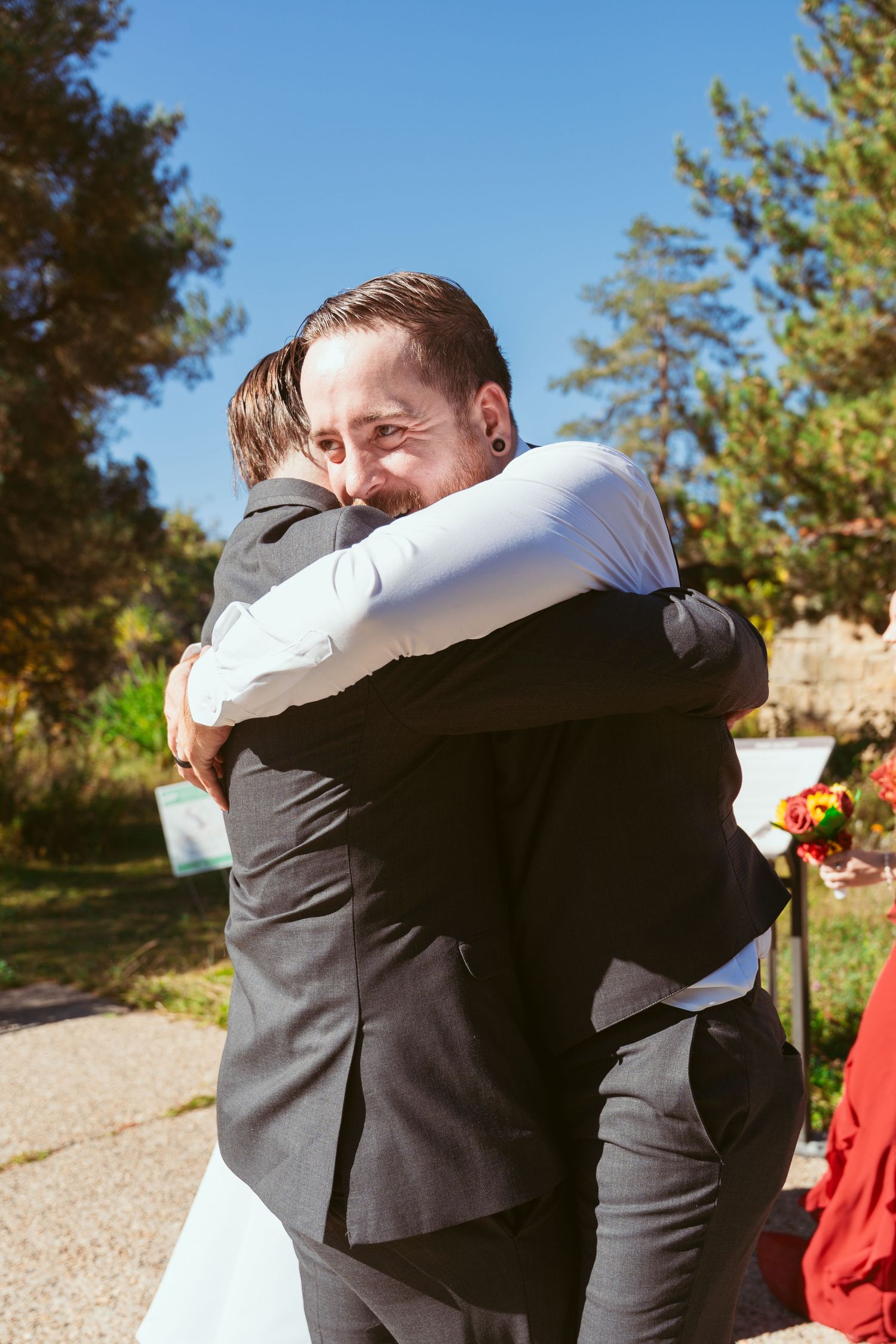Emotional embrace between two people in formal attire during an outdoor autumn wedding.