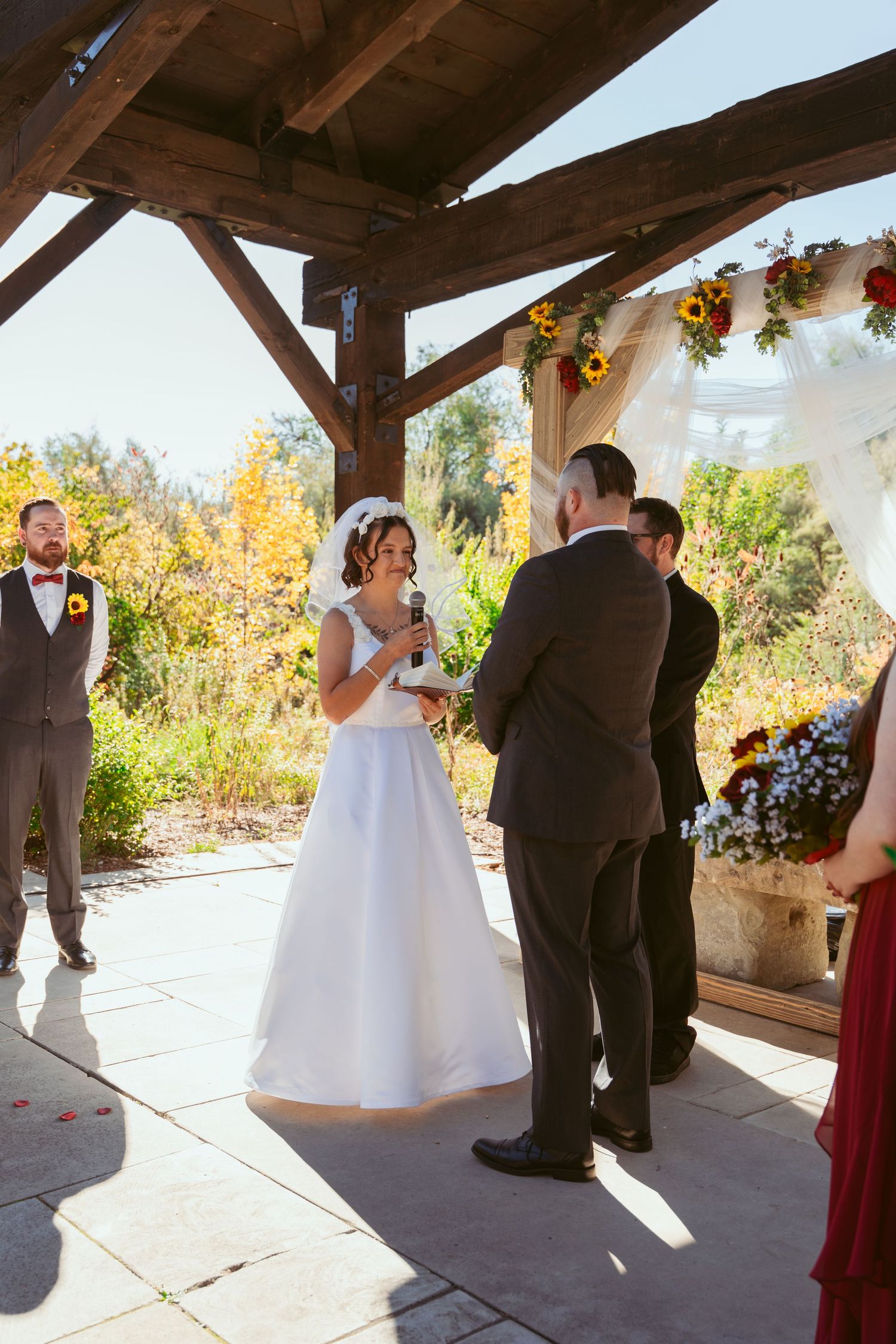 Emotional wedding ceremony taking place under a covered patio decorated with sunflowers.