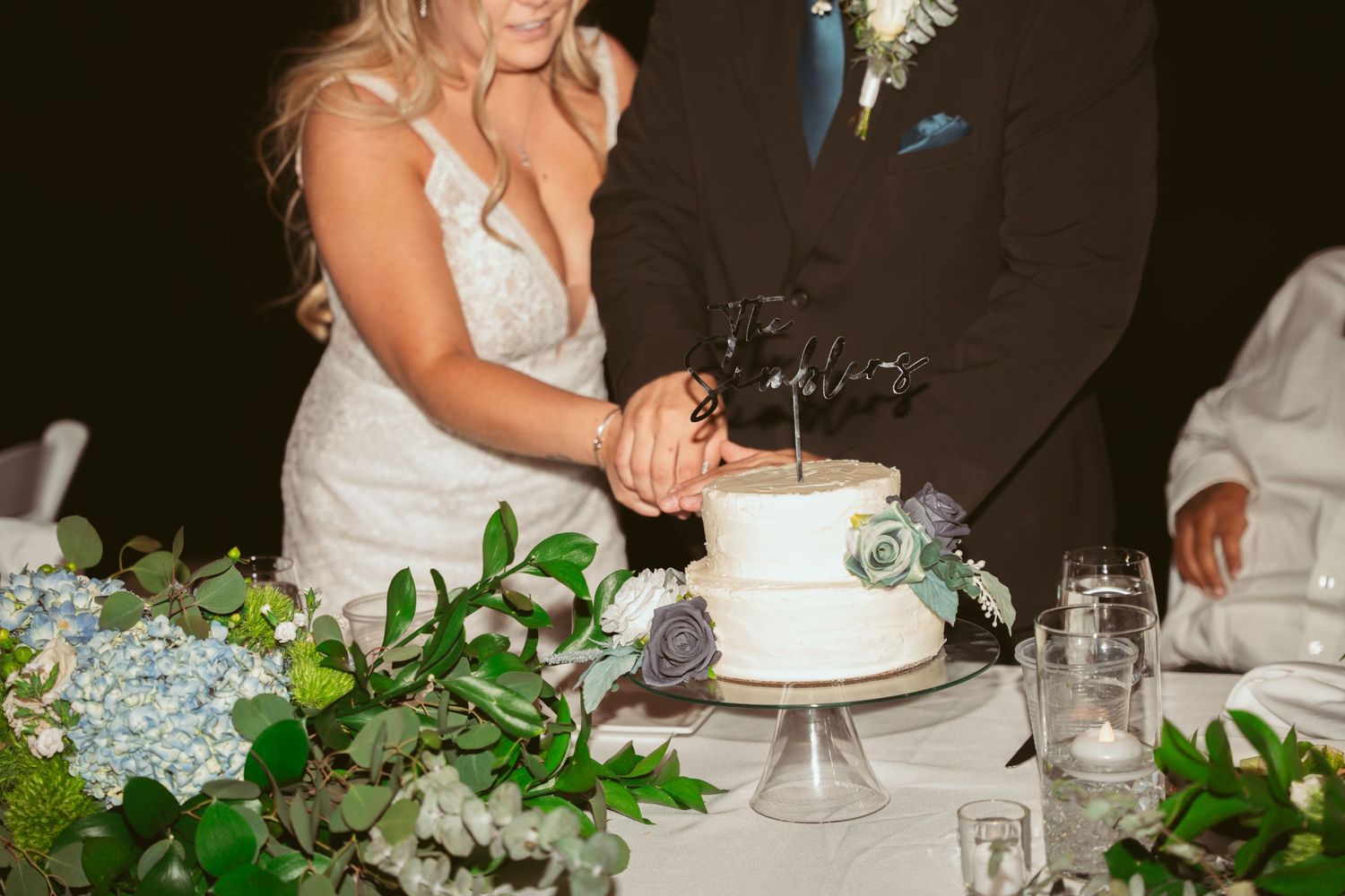 A bride and groom share a sweet moment while cutting their elegant white wedding cake at the reception.
