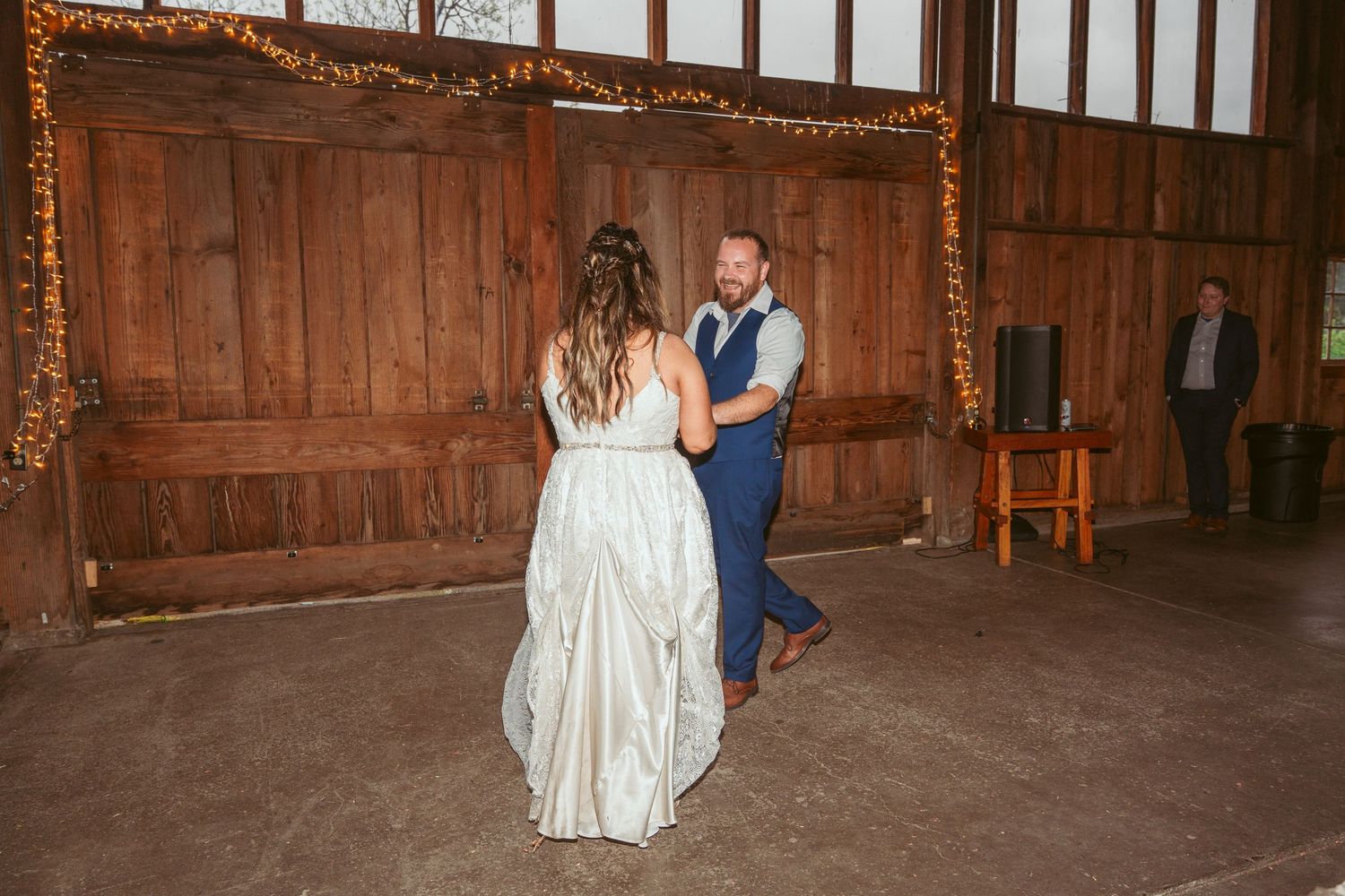 A couple dances in a rustic barn venue with wooden paneled walls.
