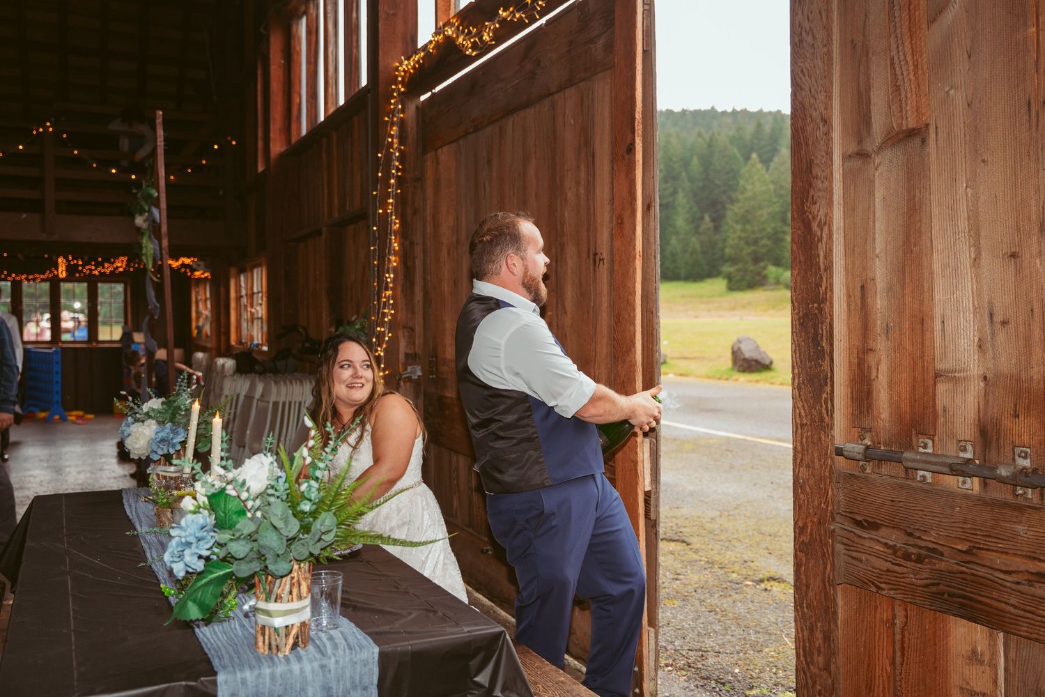 Rustic barn wedding venue decorated with string lights and floral arrangements.