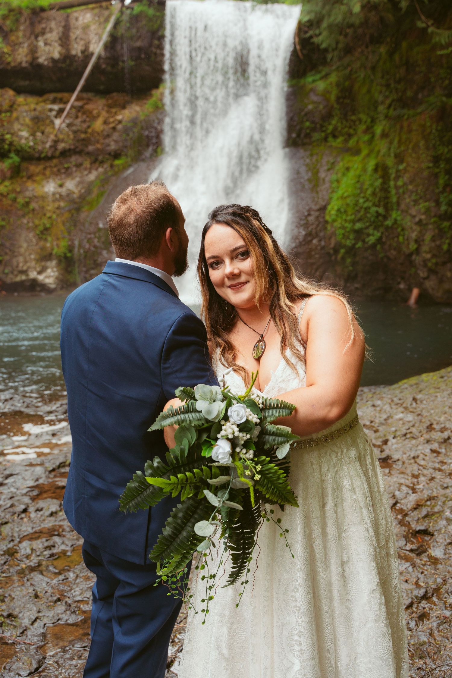 A couple shares an intimate moment in front of a cascading waterfall surrounded by lush greenery.
