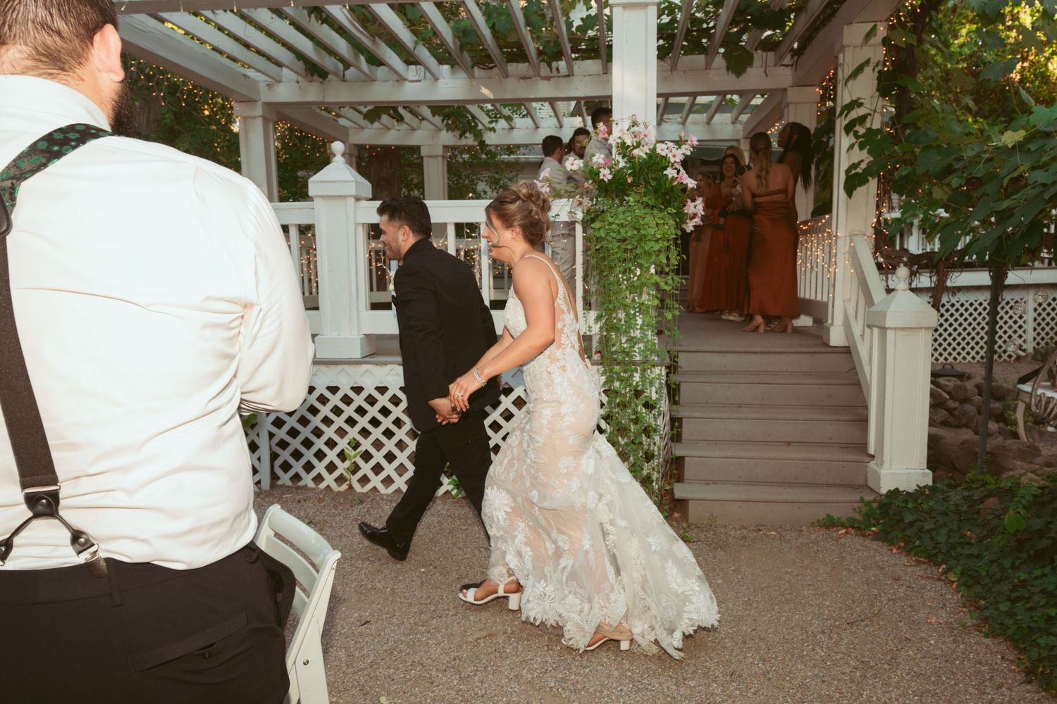 Wedding celebration with dancing guests under a white pergola decorated with climbing vines.