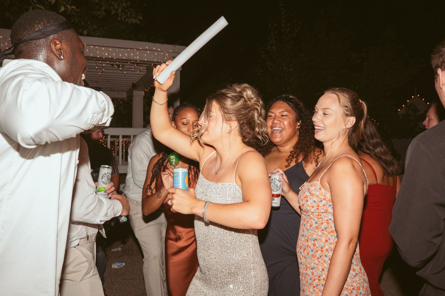 Party guests dancing and celebrating with raised drinks at a nighttime wedding reception.