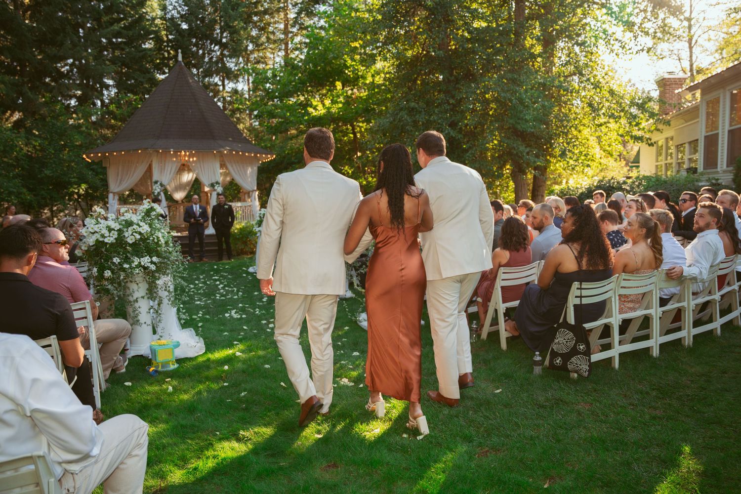 Garden wedding ceremony with white chairs and natural sunlight filtering through trees.