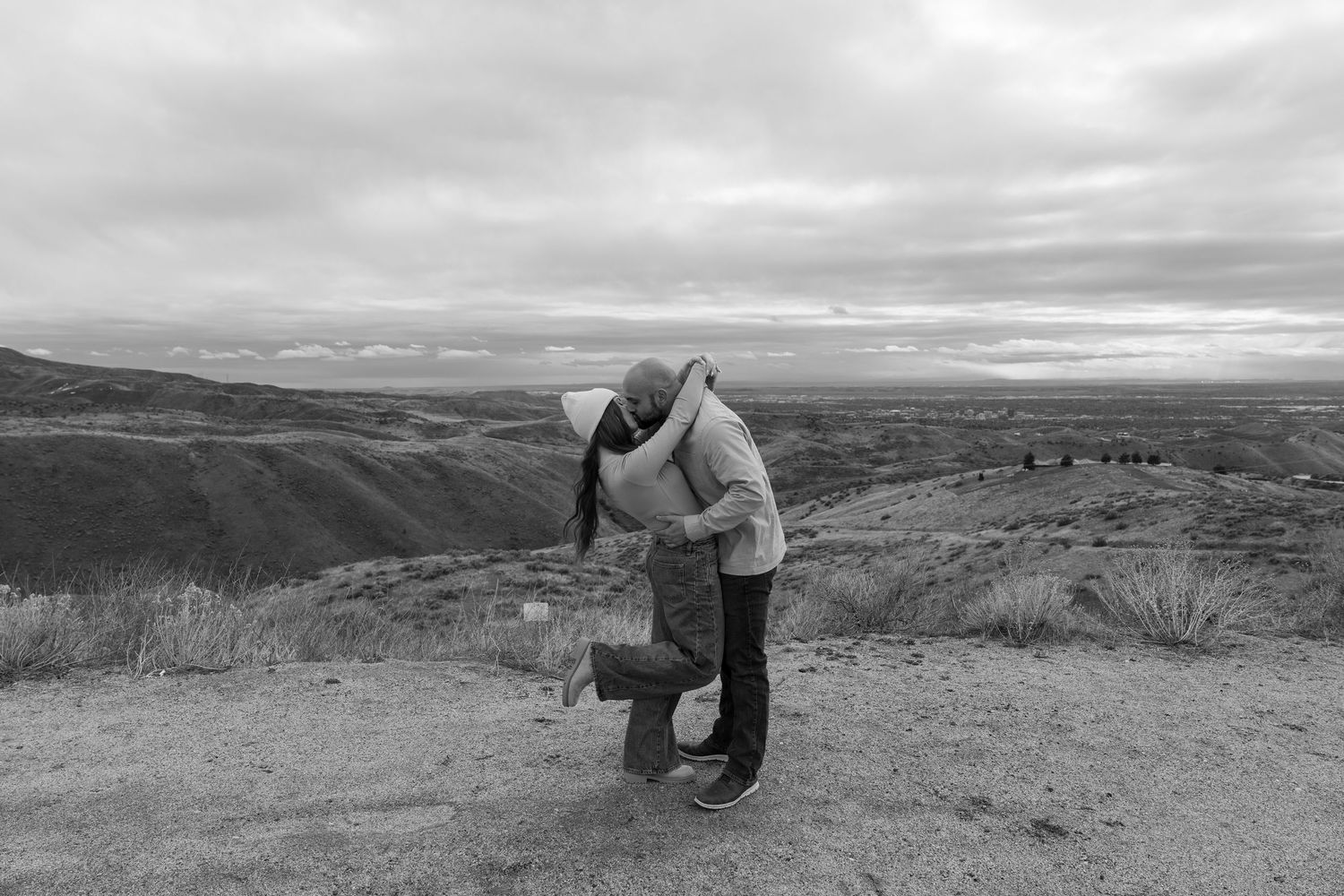 Black and white panoramic series showing a person taking photographs in a vast mountainous landscape at sunset.