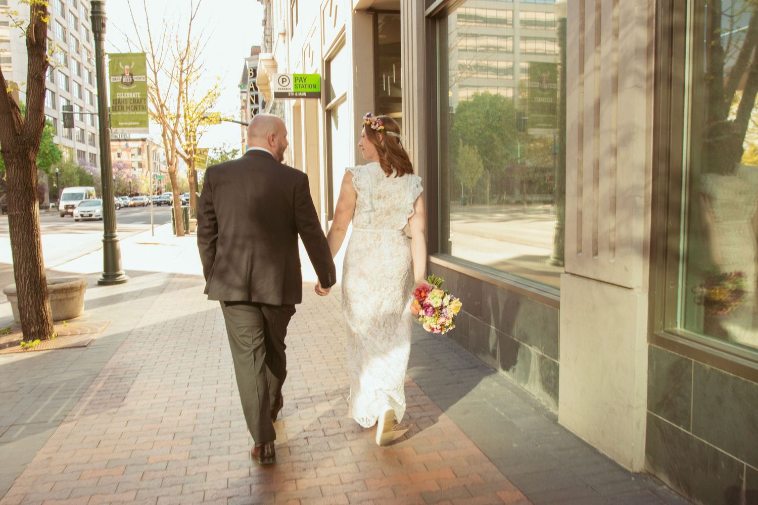 Couple walking together on a sunny urban sidewalk with modern buildings in background.