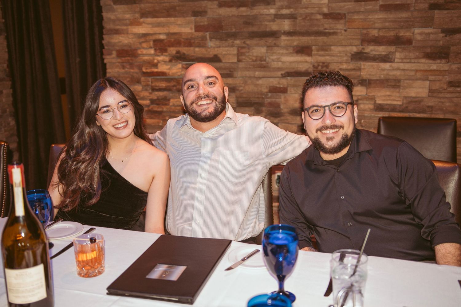 Wedding guests enjoying conversation at reception dinner with brick wall backdrop.