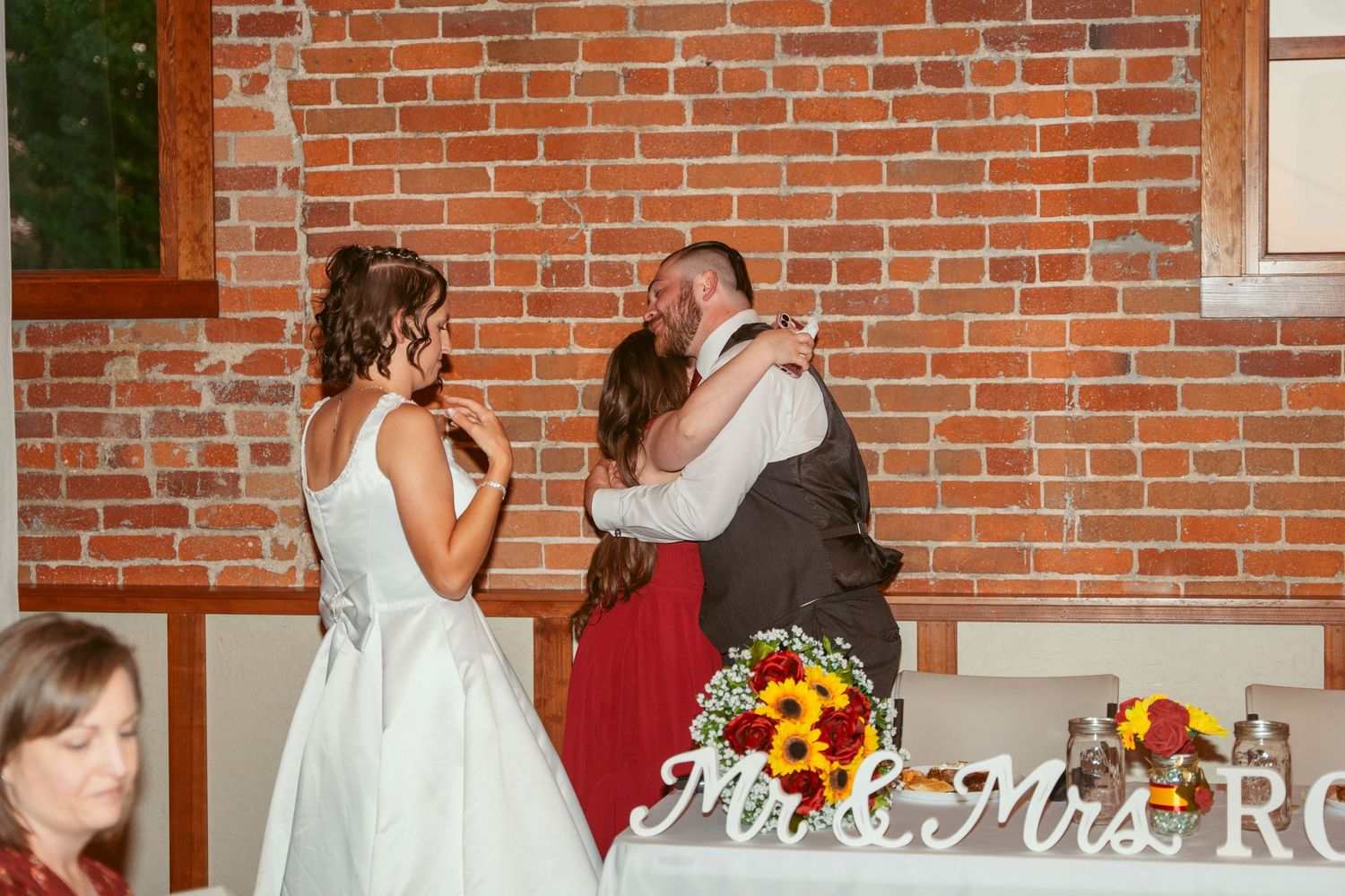 Wedding reception venue decorated with white tablecloths and floral arrangements against brick walls.