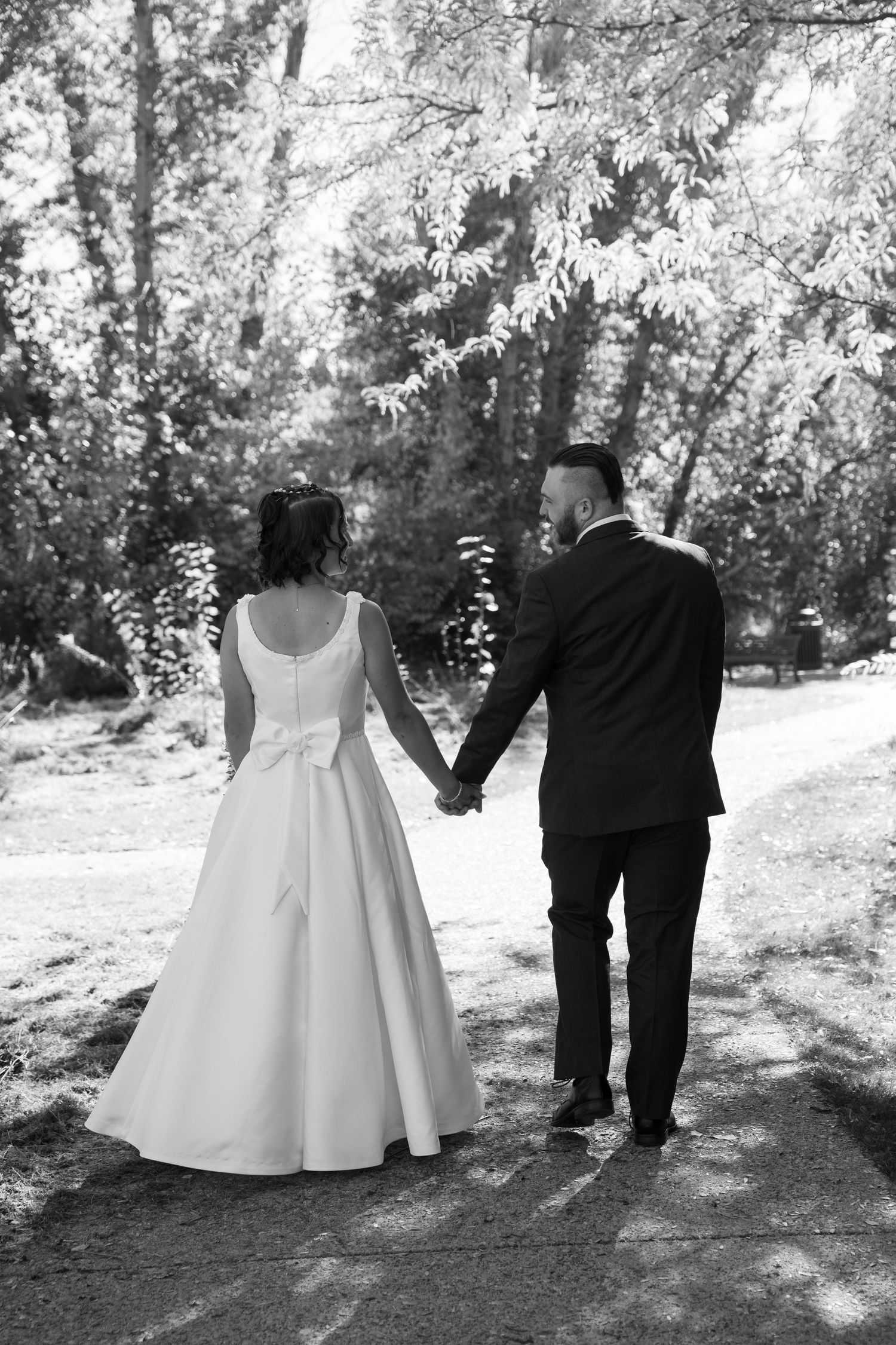 A black and white image shows a couple walking together on a sunlit forest path.