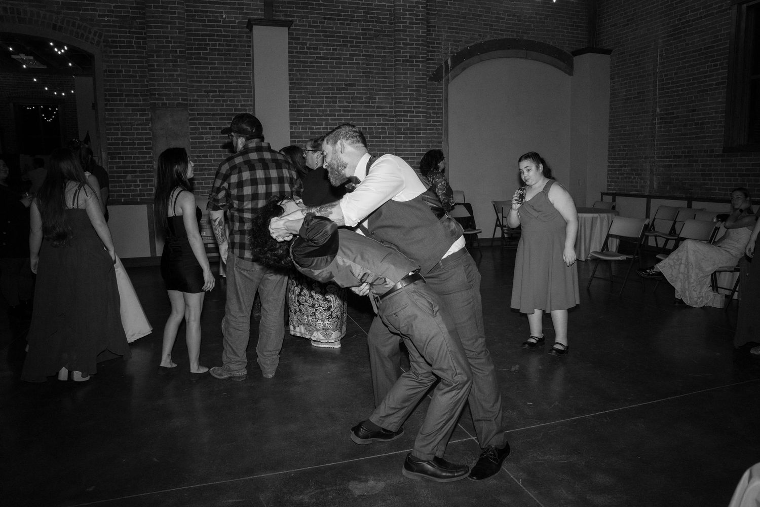 Black and white photo of dancers performing dramatic dips on a dance floor at an indoor celebration.