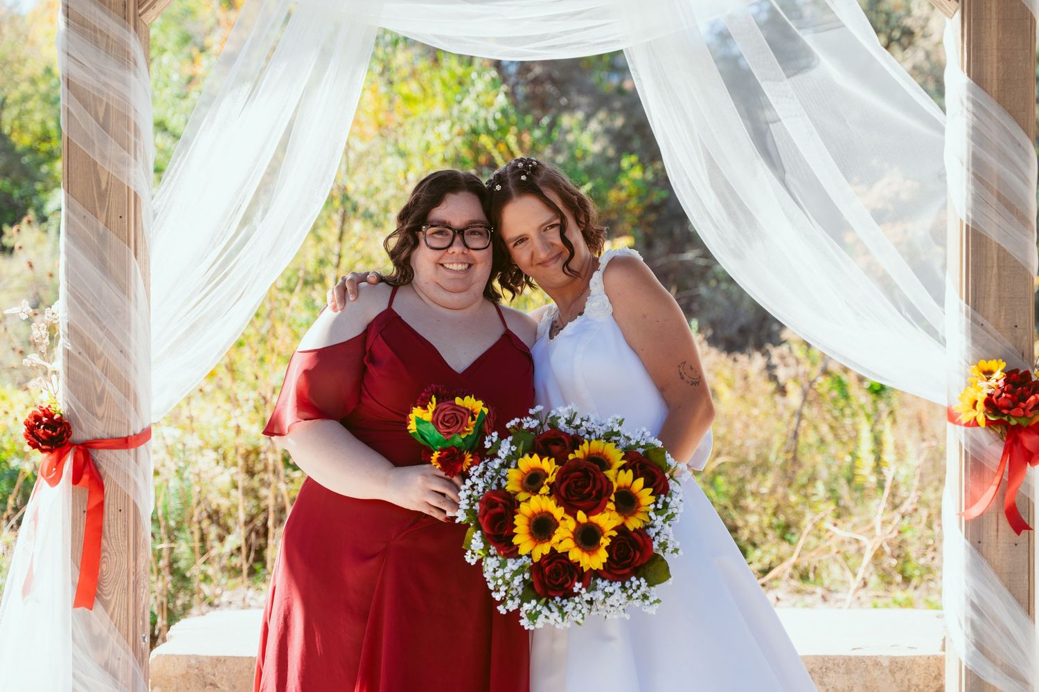 Wedding party sharing laughs under an outdoor pavilion decorated with white drapes and sunflowers.