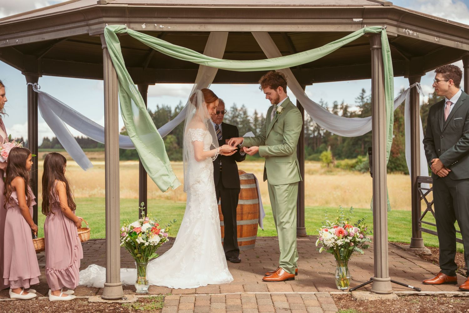 Wedding ceremony in progress under wooden gazebo with mountain landscape backdrop.