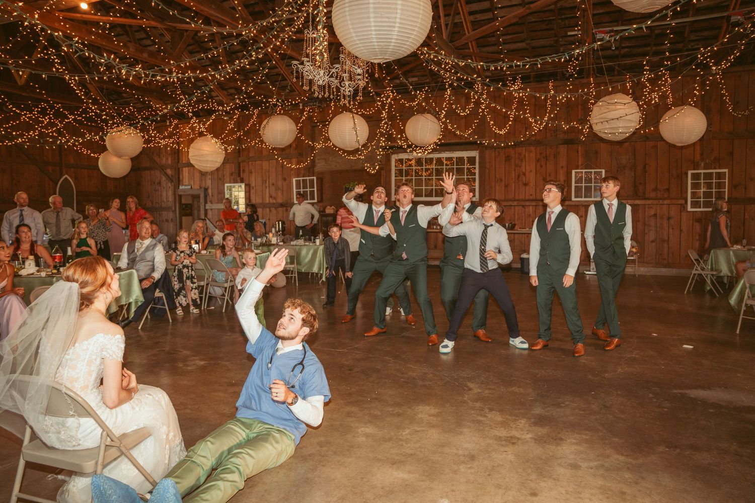 Wedding party members performing choreographed dance routine in decorated barn venue.