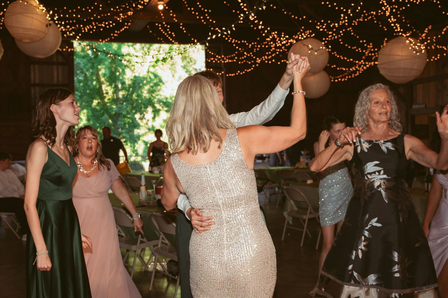 Wedding guests dancing and celebrating in a beautifully lit barn venue with natural light.
