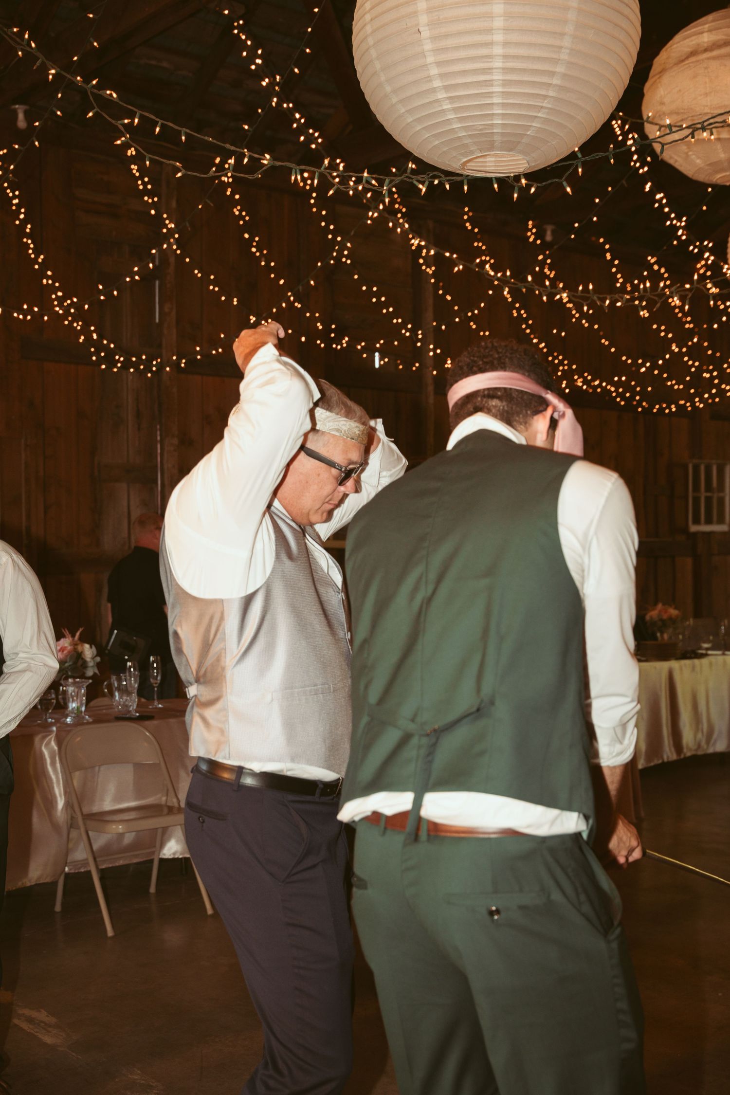 Groomsmen in vests and dress shirts dancing at a barn wedding reception.
