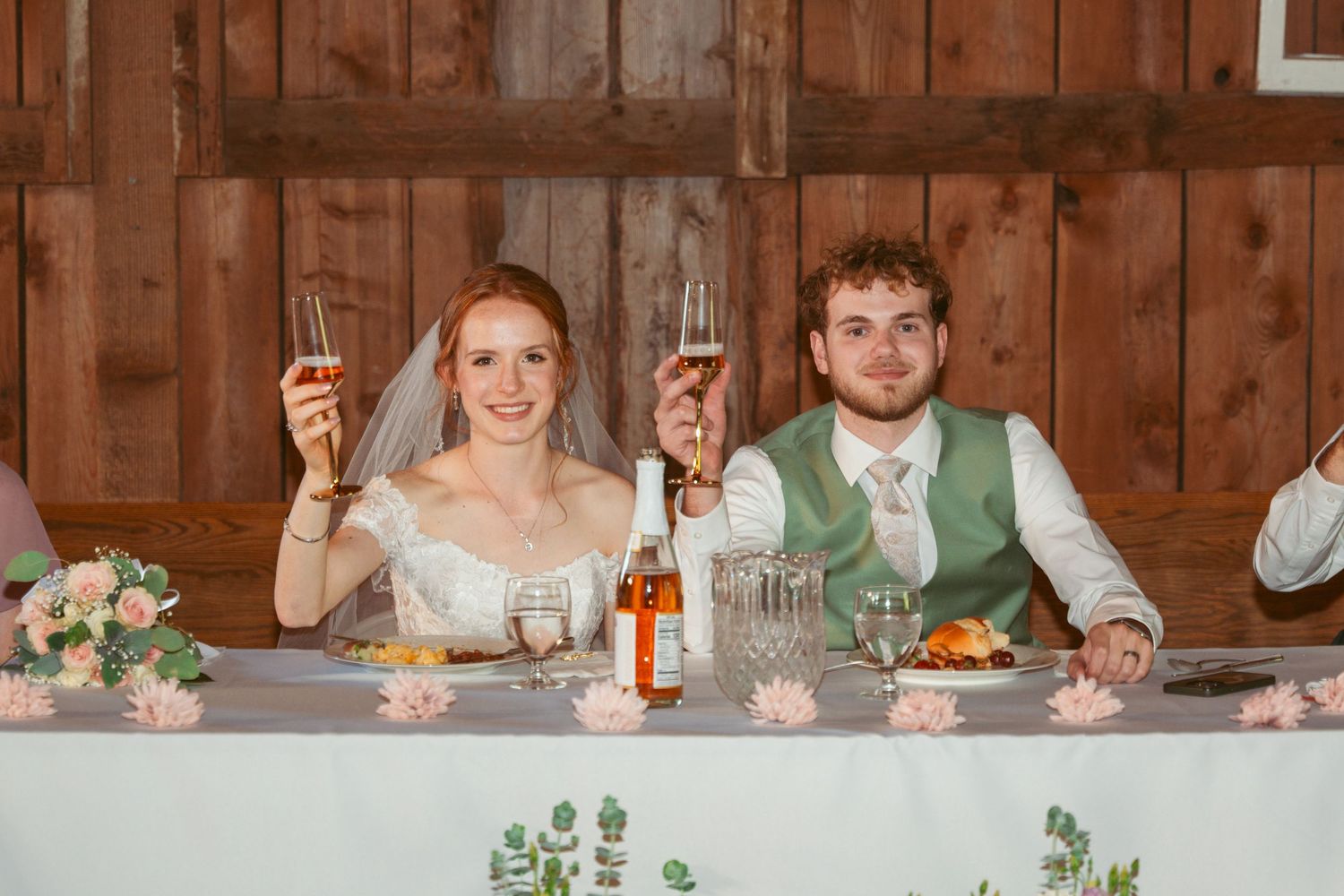 Wedding reception head table with floral arrangements and place settings in rustic barn.