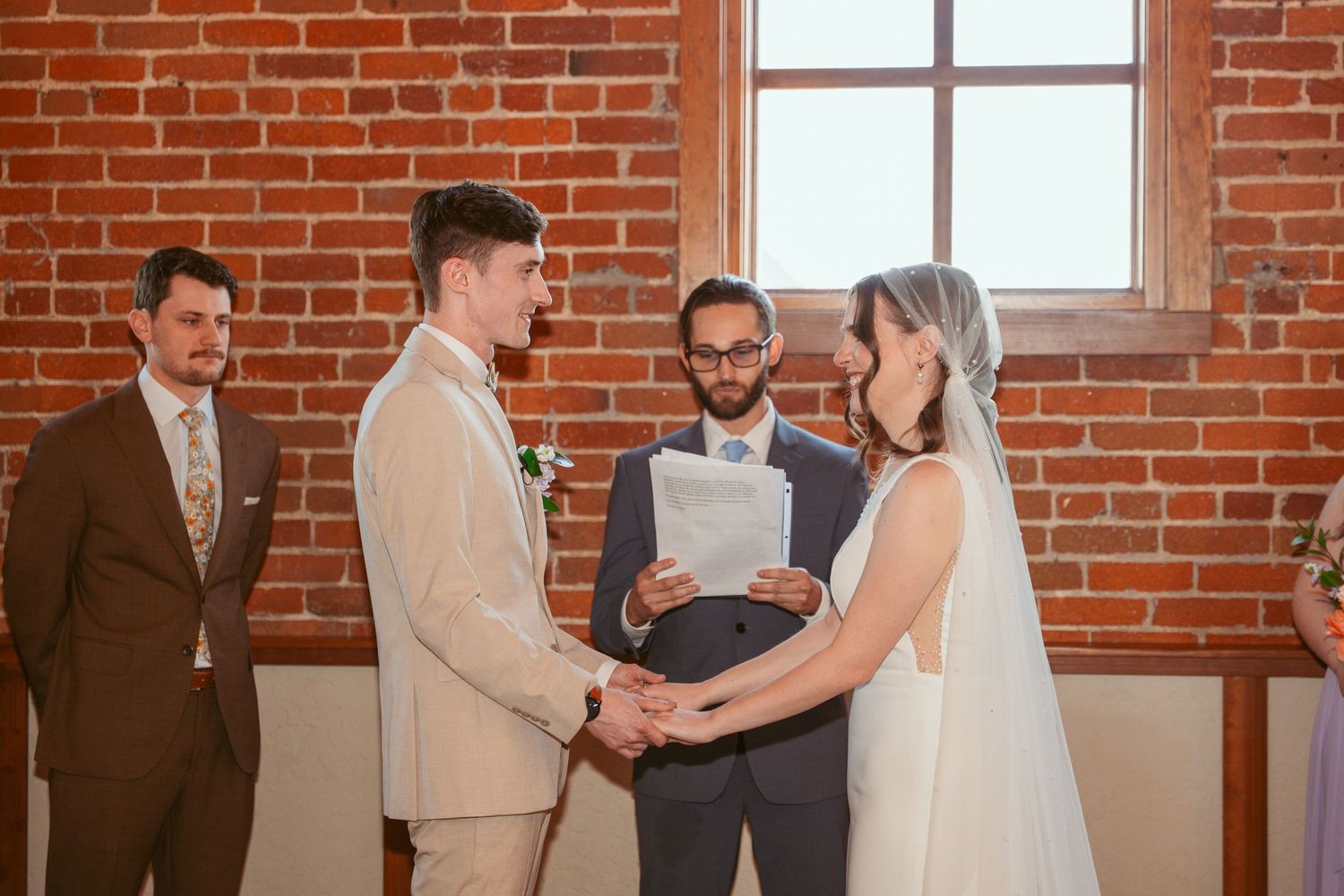 Wedding ceremony in a rustic brick venue with guests watching the couple exchange vows at the altar.