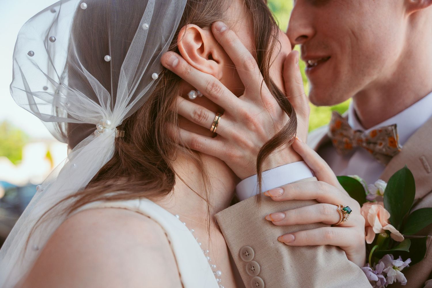 Close-up detail of tender embrace showing wedding rings and delicate veil.