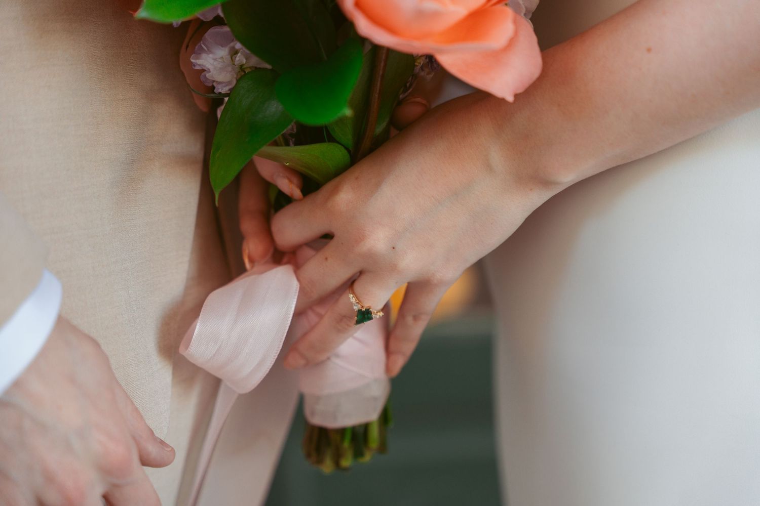 Close-up of hands holding wedding bouquet with engagement ring.